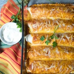 Enchiladas in a baking dish next to a small bowl of sour cream.