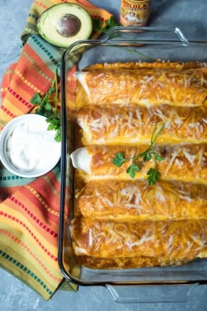 Enchiladas in a baking dish next to a small bowl of sour cream.