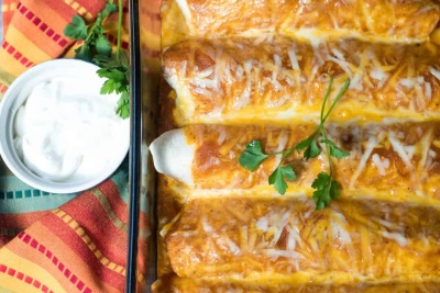 Enchiladas in a baking dish next to a small bowl of sour cream.