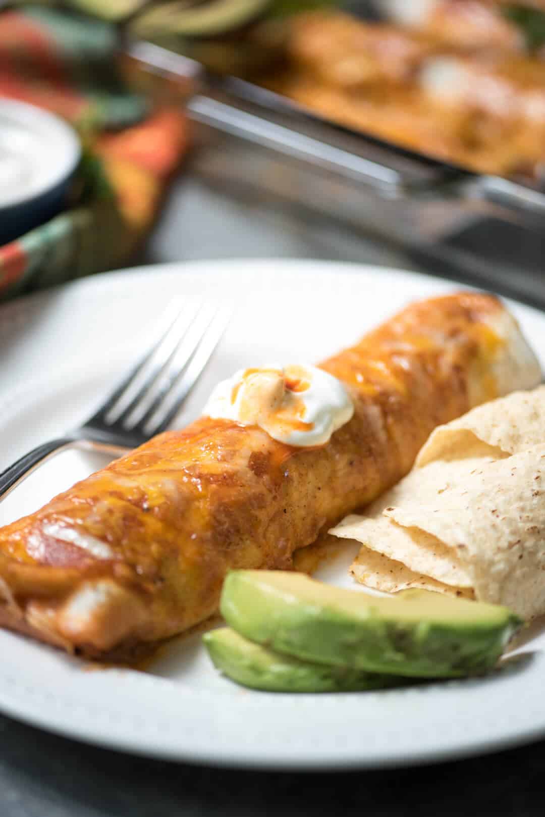 An enchilada on a plate topped with sour cream.