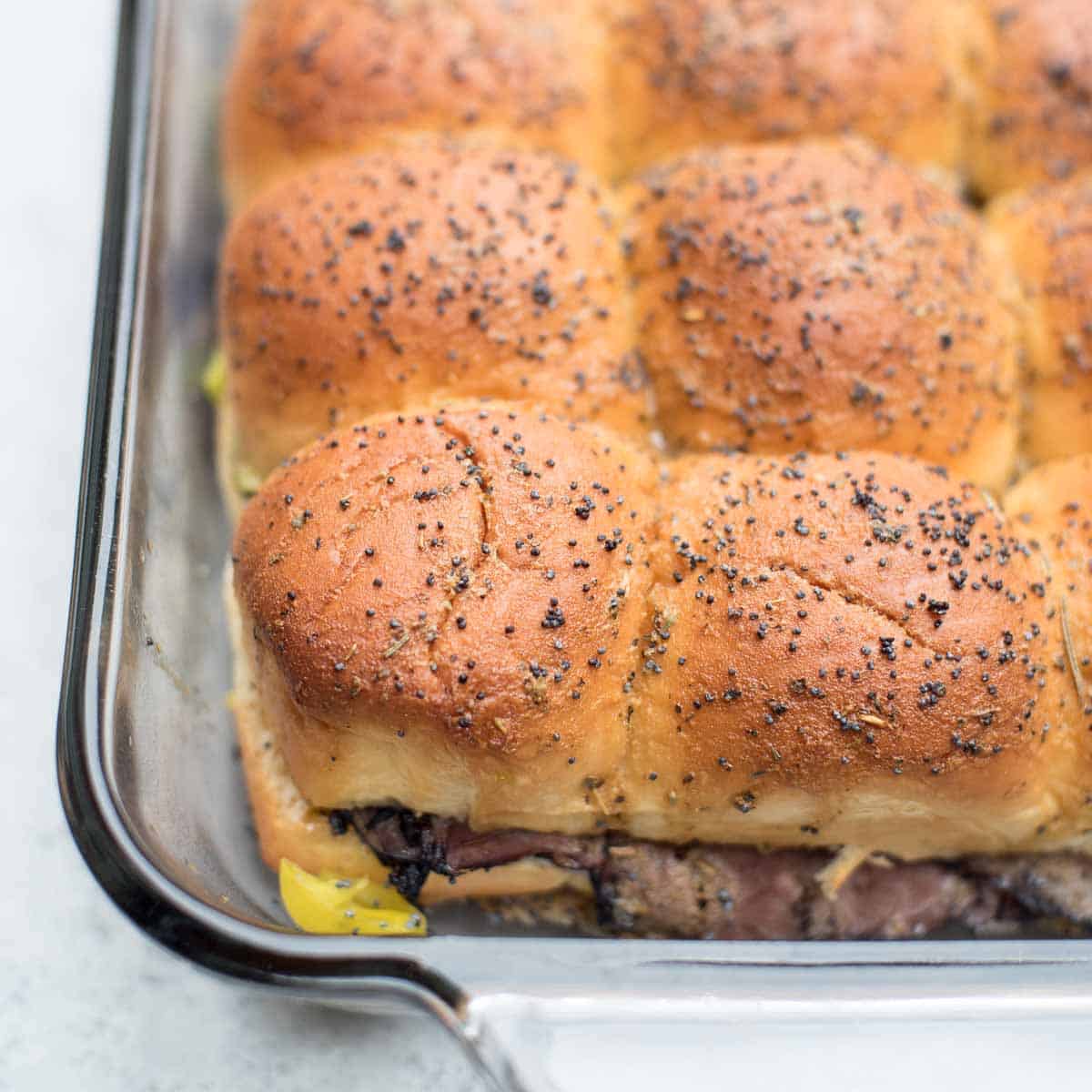 Roast beef sliders with pepperoncini in a baking dish.