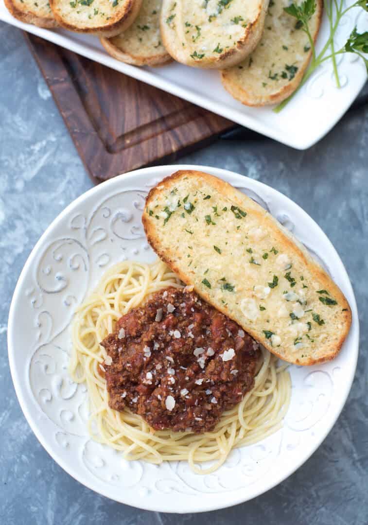 An over the top image of a piece of the garlic bread with spaghetti in a white bowl.