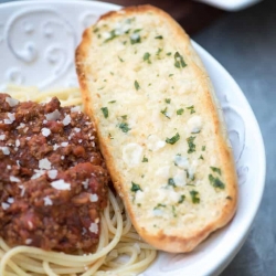 A piece of garlic bread on a plate with spaghetti.