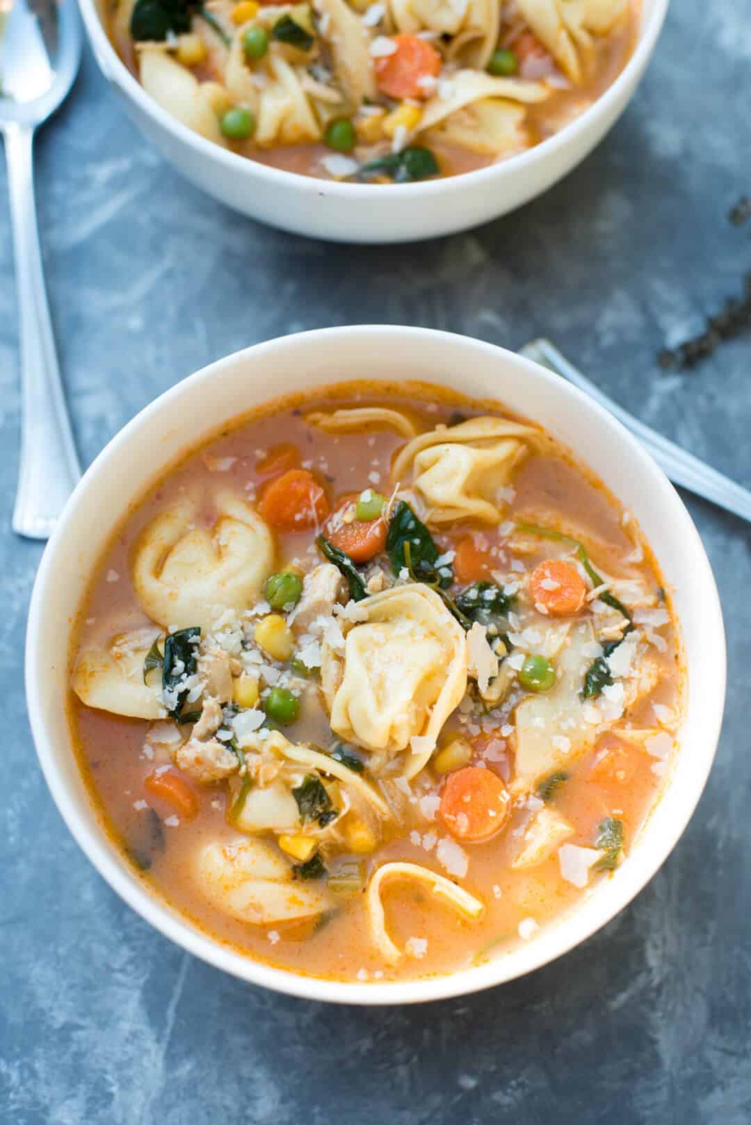 A white bowl full of Chicken Vegetable Tortellini Soup on a grey surface.