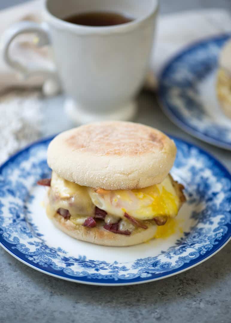A corned beef breakfast sandwich on an English muffin on a blue and white plate.