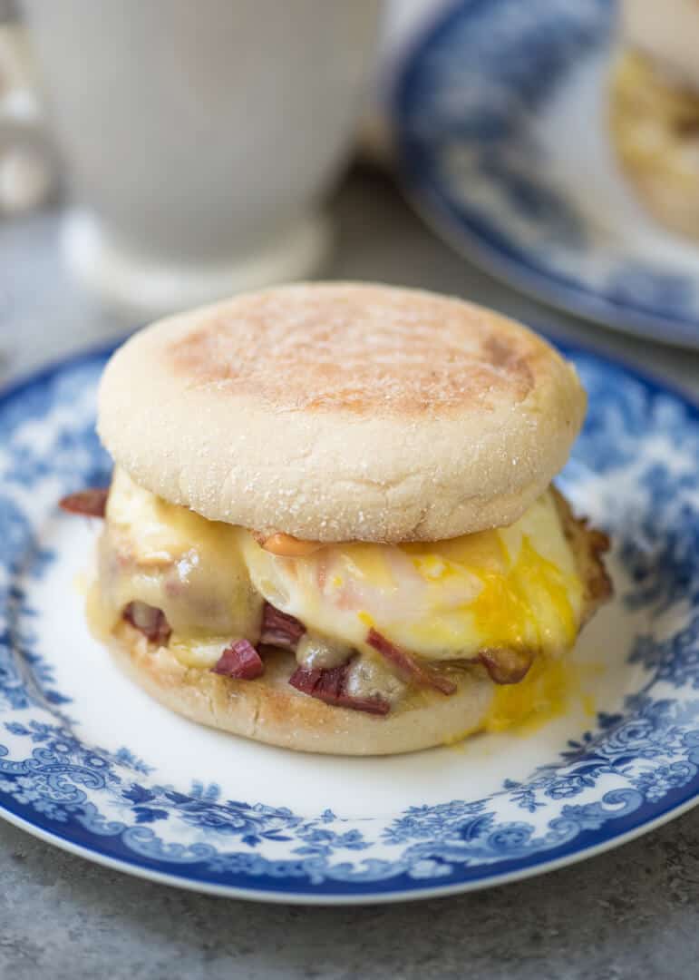 A close up of a breakfast sandwich on an English muffin with corned beef, an egg and melted cheese.