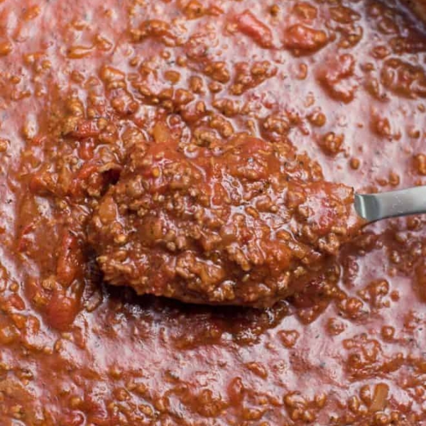 A close up of a spoon lifting homemade spaghetti sauce from a pot.