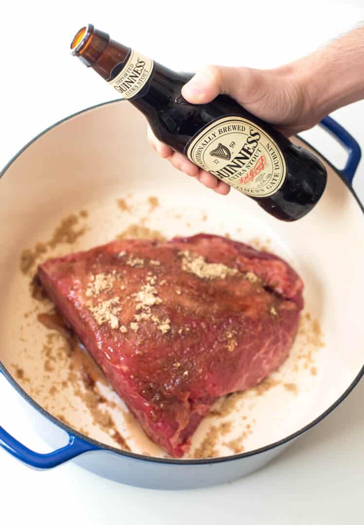 A bottle of Guinness Draught hovering above a pot with corned beef.