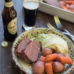 Slices of corned beef, carrots, and cabbage in a bowl with a bottle of Guinness.