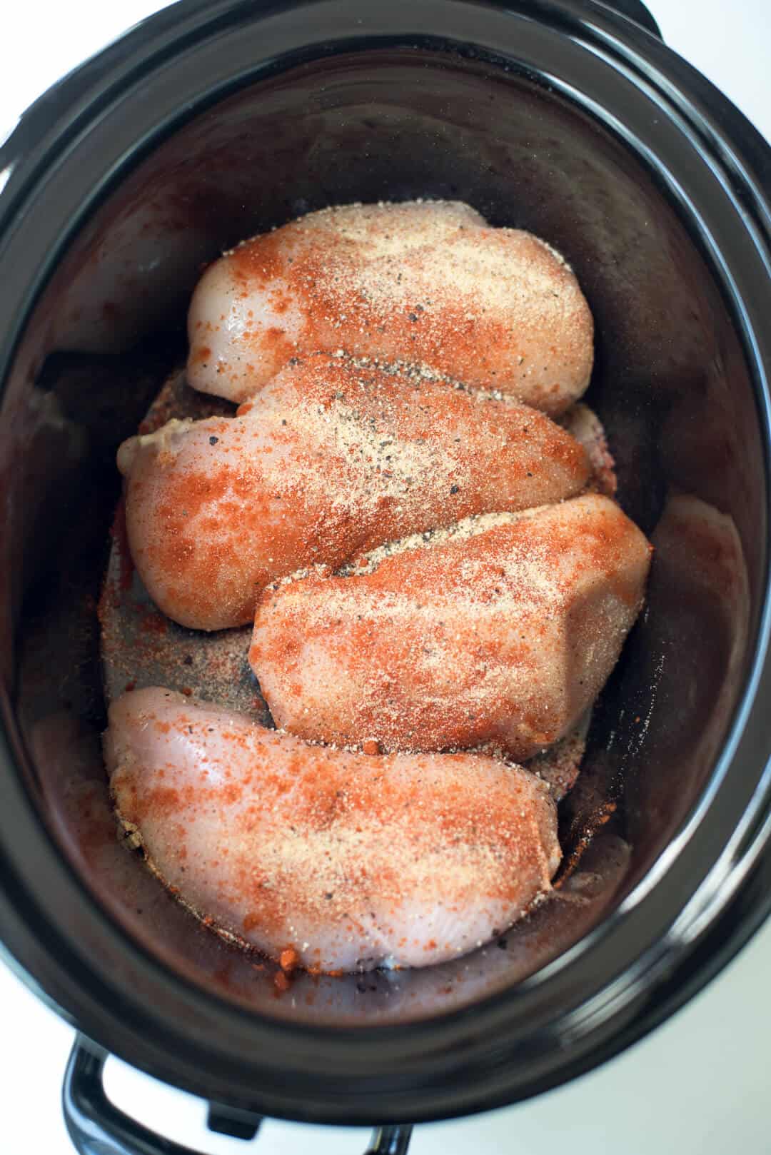 Seasoned chicken breasts in a slow cooker insert.