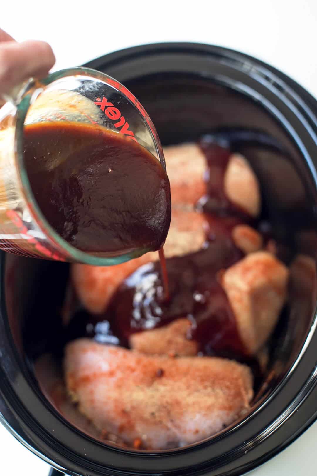 BBQ sauce is poured over the chicken in the slow cooker.