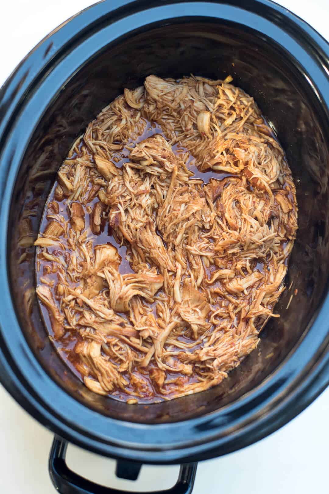The chicken is shredded into the sauce in the slow cooker.