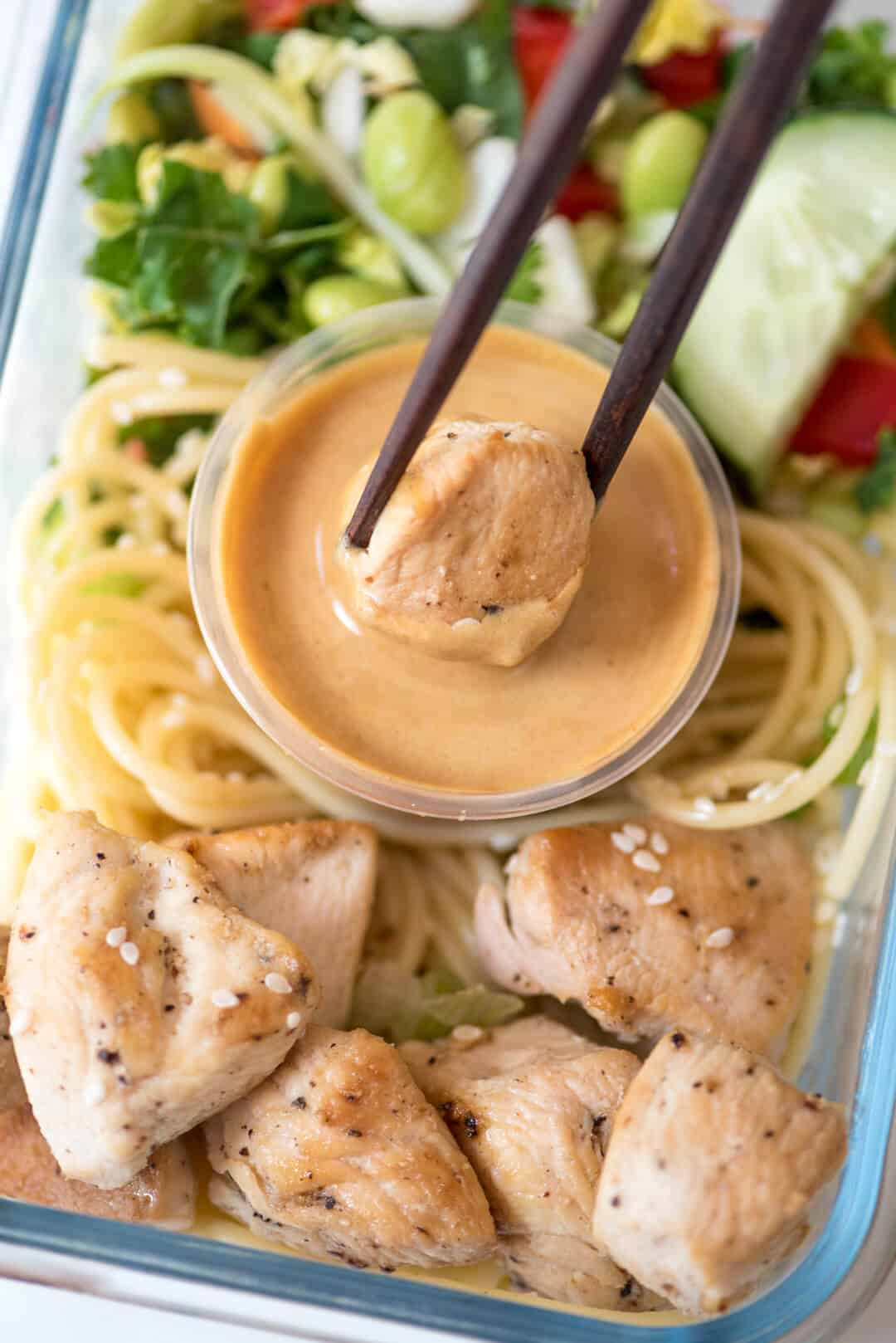 Chopsticks dip a piece of chicken into peanut sauce.