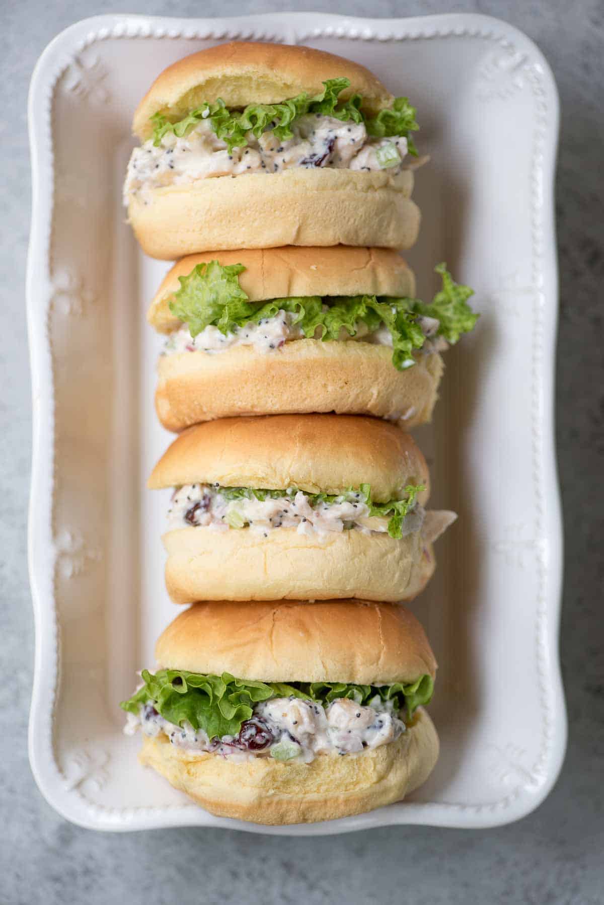 Cranberry chicken salad sandiwches on small buns in a white dish.