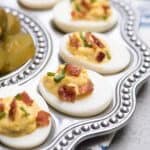 Deviled eggs topped with crumbled bacon and chives on a silver platter.