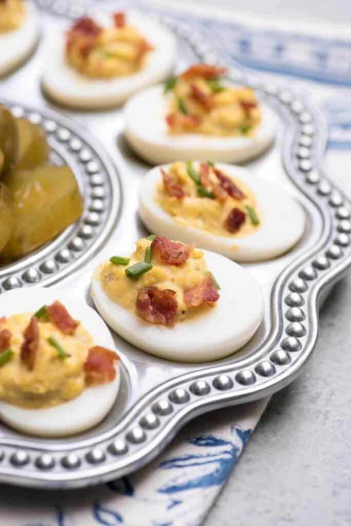 Deviled eggs topped with crumbled bacon and chives on a silver platter.