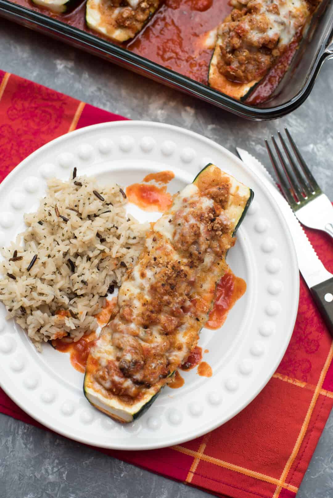 An Italian Stuffed Zucchini Boat on a white serving plate with rice.