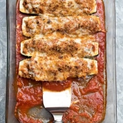 A spatula scoops up a zucchini boat from a casserole dish.