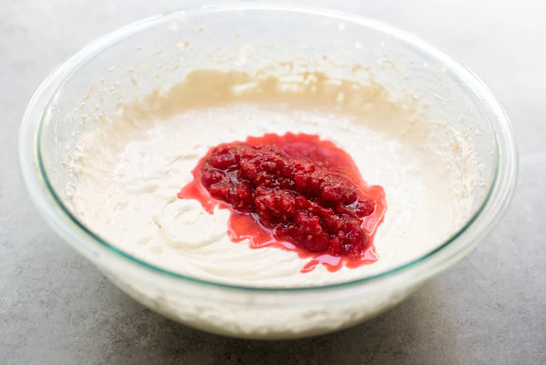 Smashed fresh raspberries combined with sugar are added to the mixing bowl.