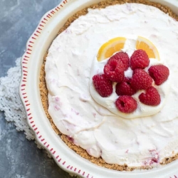 A piece pie topped with whipped cream, lemon slices and raspberries.