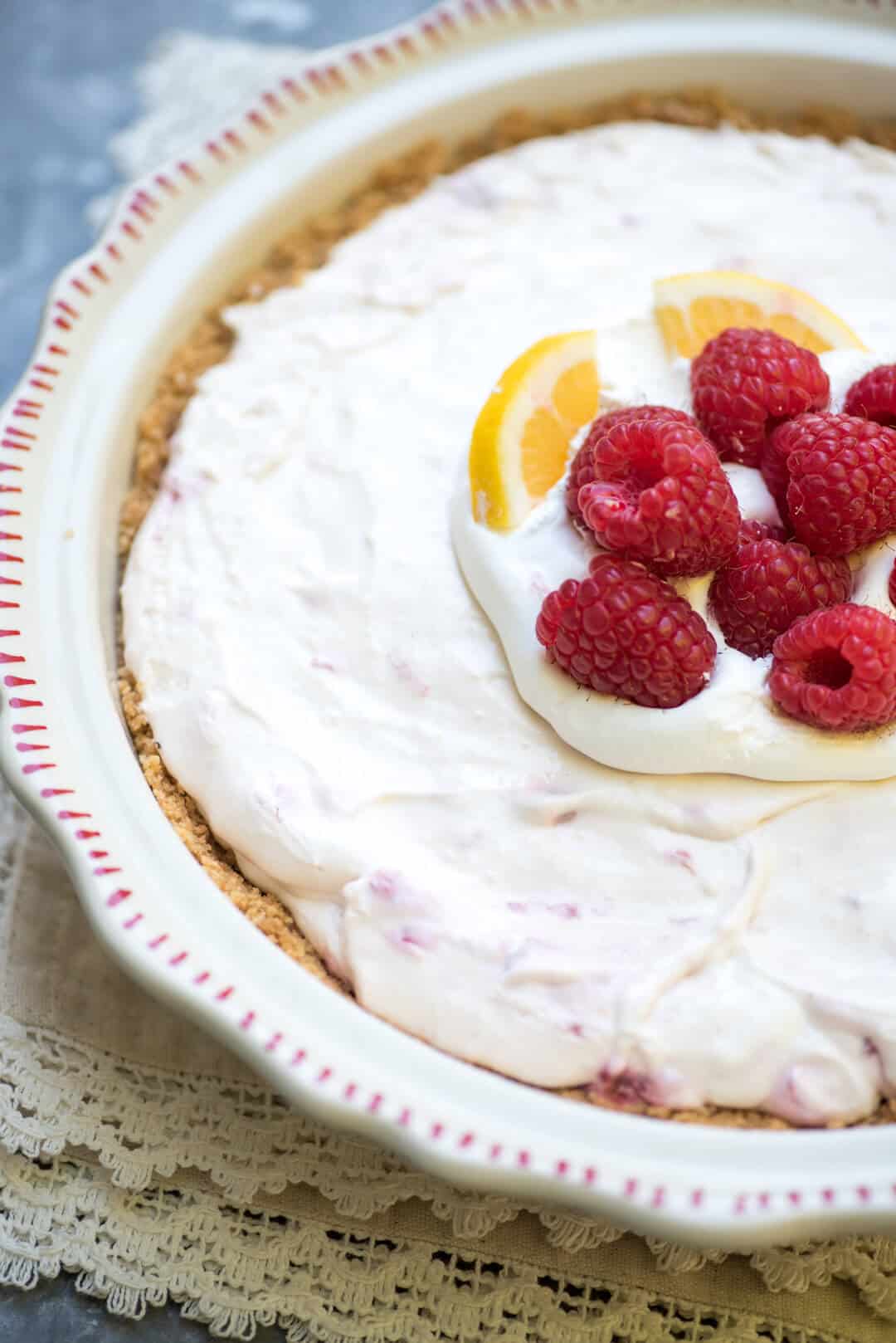 A closeup of the pie in the pie plate decorated with raspberries and lemon slices.
