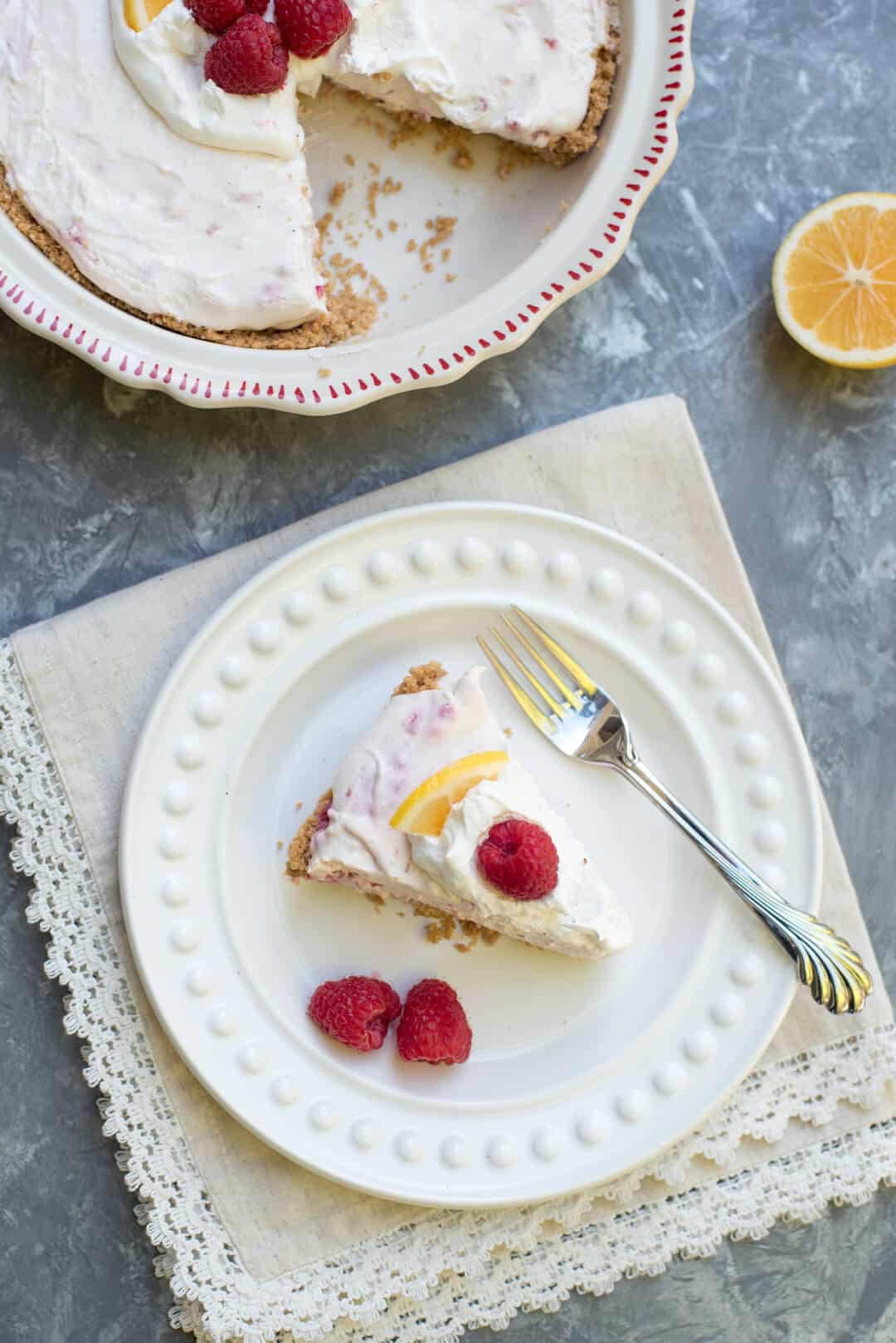 An over the top shot of a slice of Lemon Raspberry Pie on a white plate with raspberries.