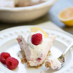 A close up of a piece of Creamy Lemon Raspberry Pie on a plate with a fork.