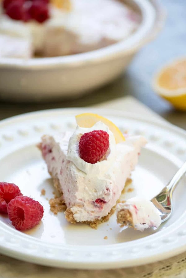 A close up of a piece of Creamy Lemon Raspberry Pie on a plate with a fork.