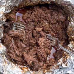 Two forks shredding beef in foil.