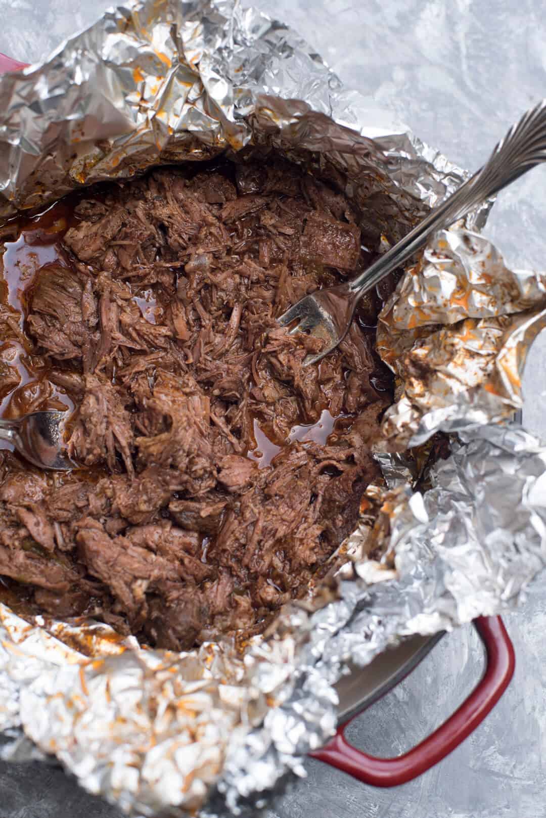 A fork stuck into Shredded Mexican Beef in a foil lined pan.