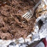 A fork stuck in Shredded Mexican Beef in a foil lined pan.