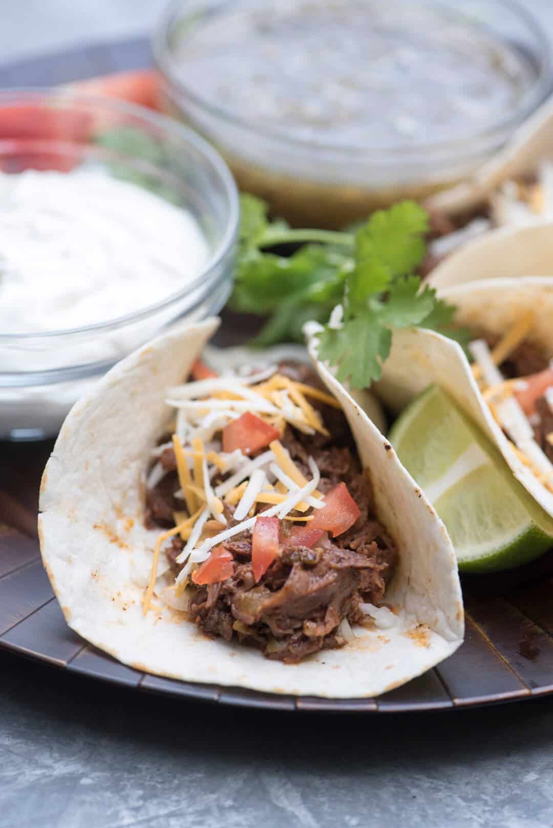 Shredded beef tacos on a platter with a small bowl of sour cream.