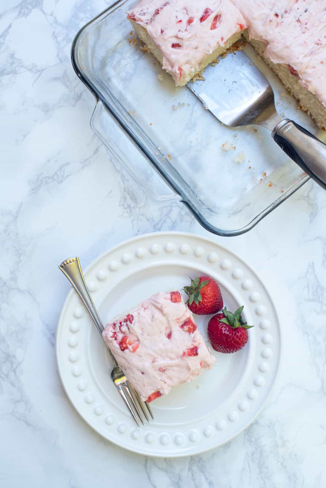 A slice of the cake on a white plate with strawberries and fork shot from over the top.