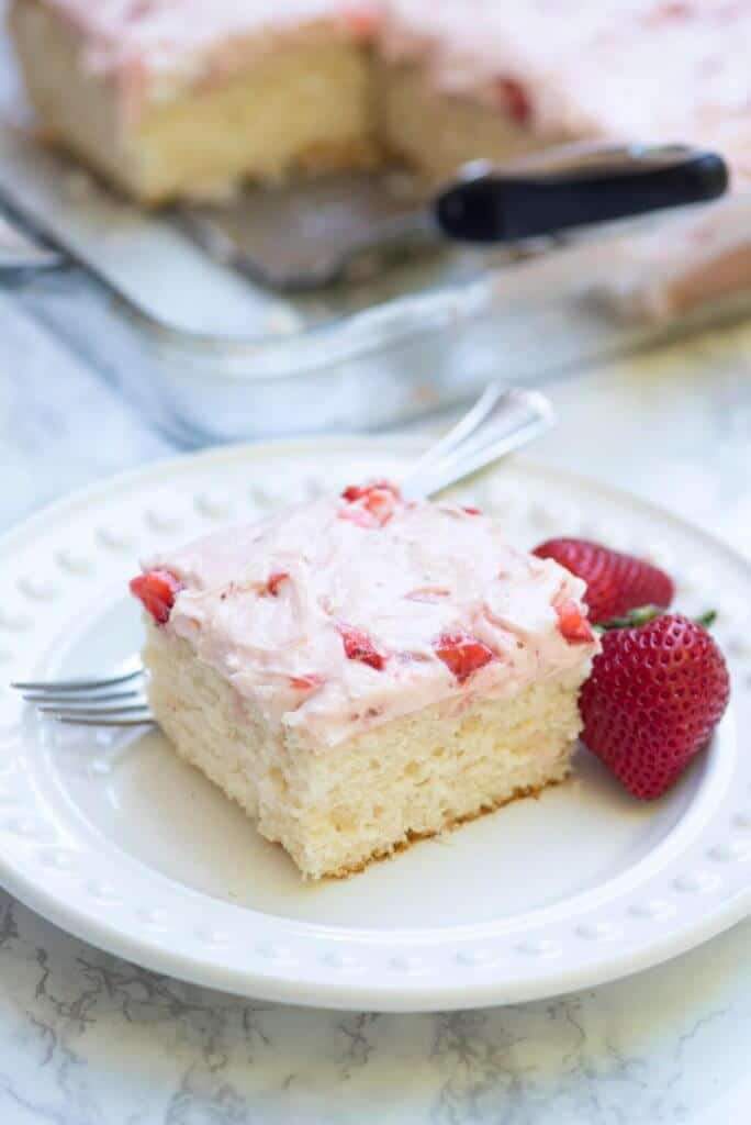 A close up of a slice of 7up sheet cake with strawberry frosting on a plate.