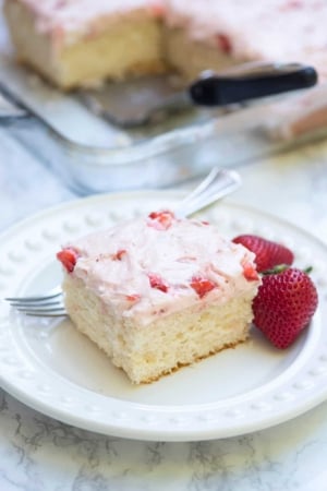 A close up of a slice of 7up sheet cake with strawberry frosting on a white plate with a fork.