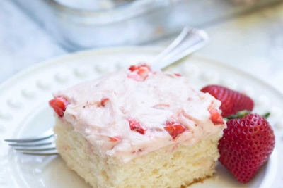 A close up of a slice of 7up sheet cake with strawberry frosting on a white plate with a fork.