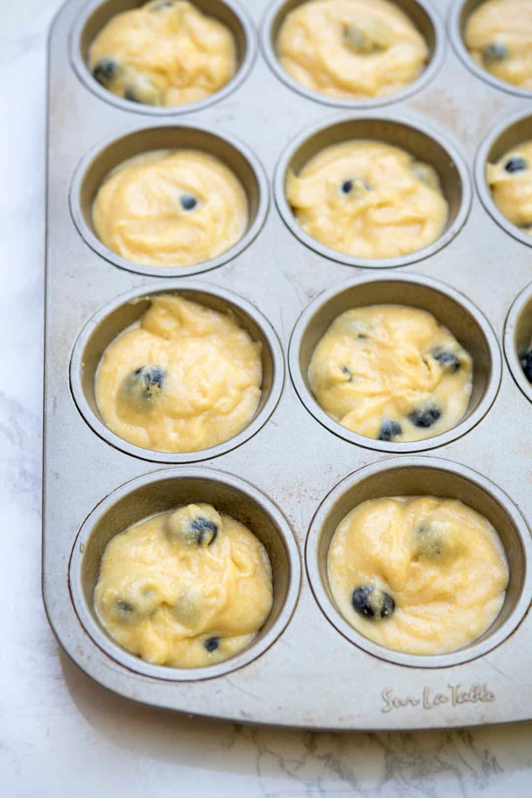 Blueberry muffin batter in a muffin pan.