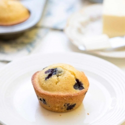 A blueberry cornmeal muffin on a white plate.