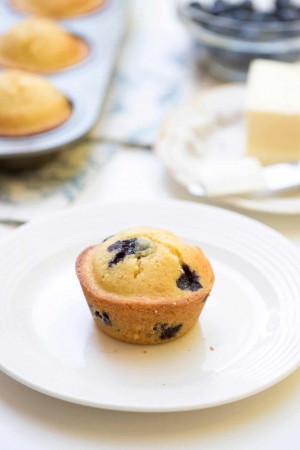 A blueberry cornmeal muffin on a white plate.