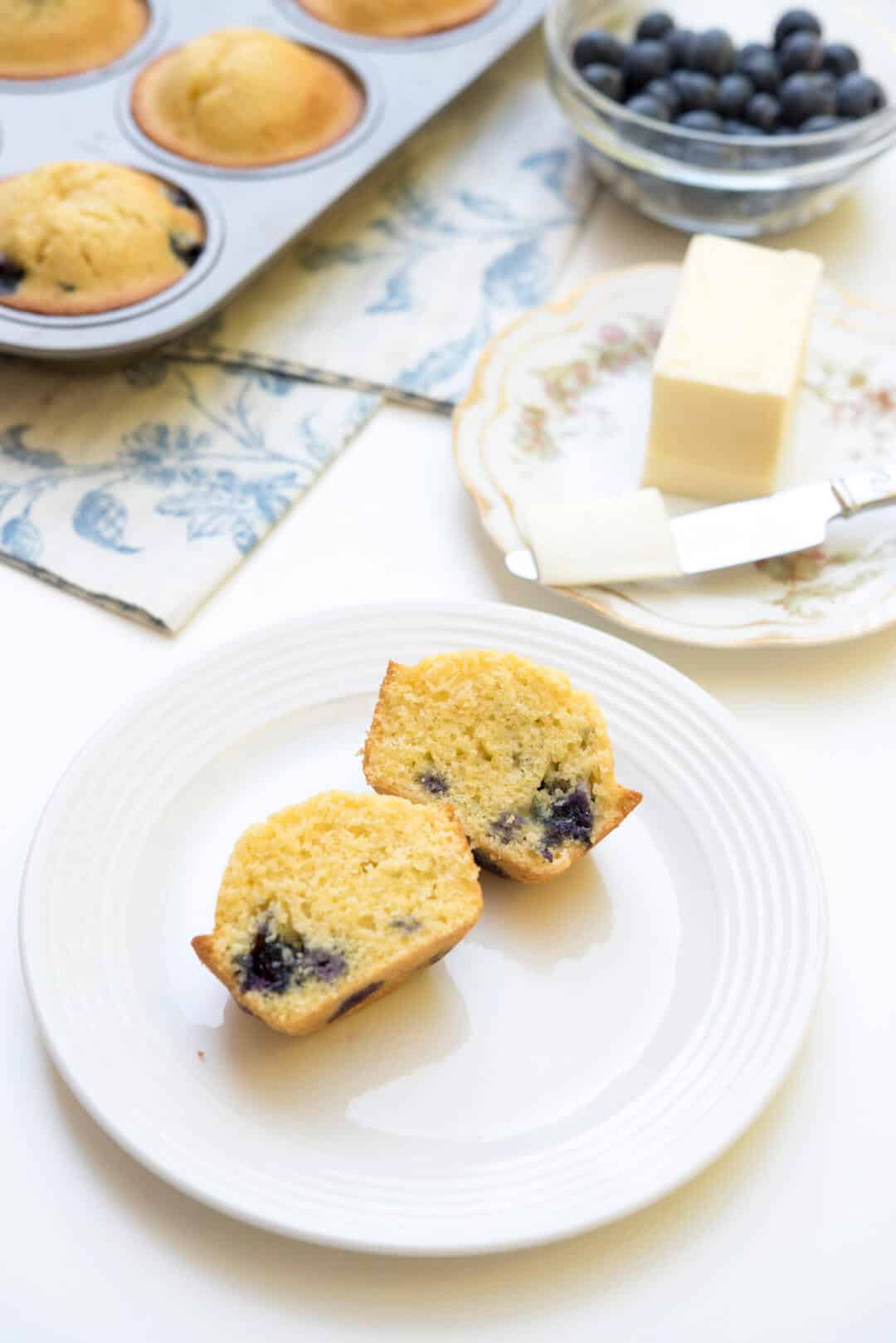 A Blueberry Cornmeal Muffin sliced in half on a white plate.