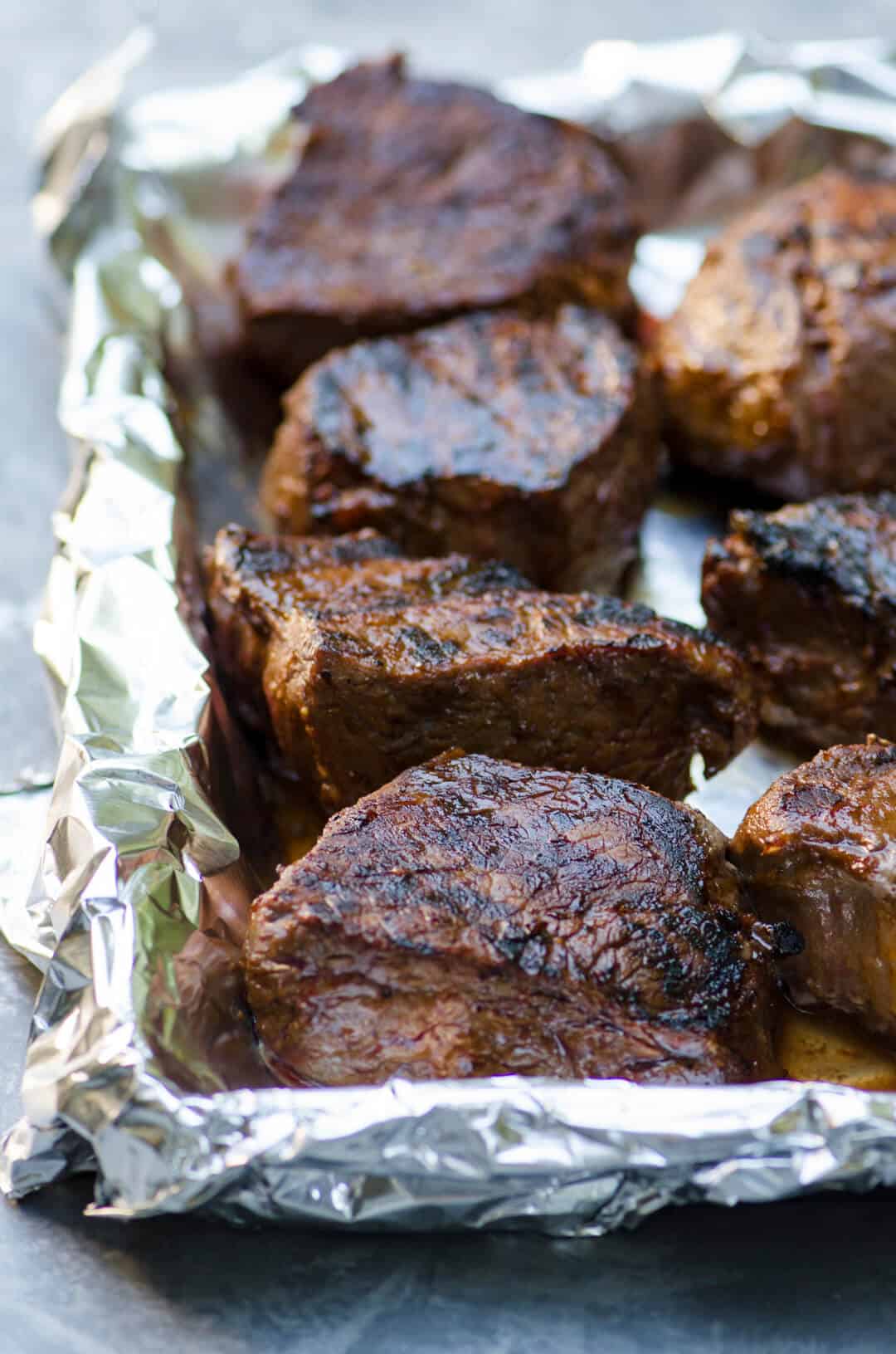 Pieces of grilled steak on a foil lined baking sheet.