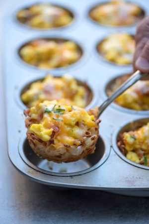 A fork lifts a hash brown and scrambled egg cup from a muffin tin.