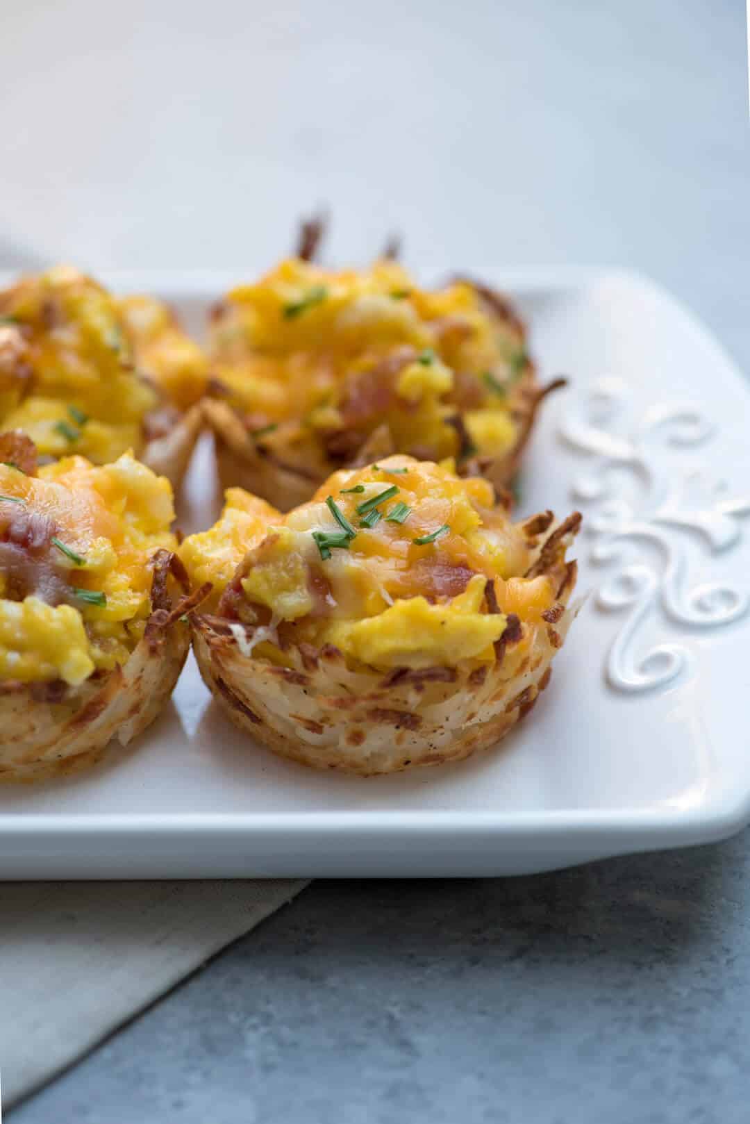 Crispy hash brown cups filled with a scrambled egg mixture on a white tray.