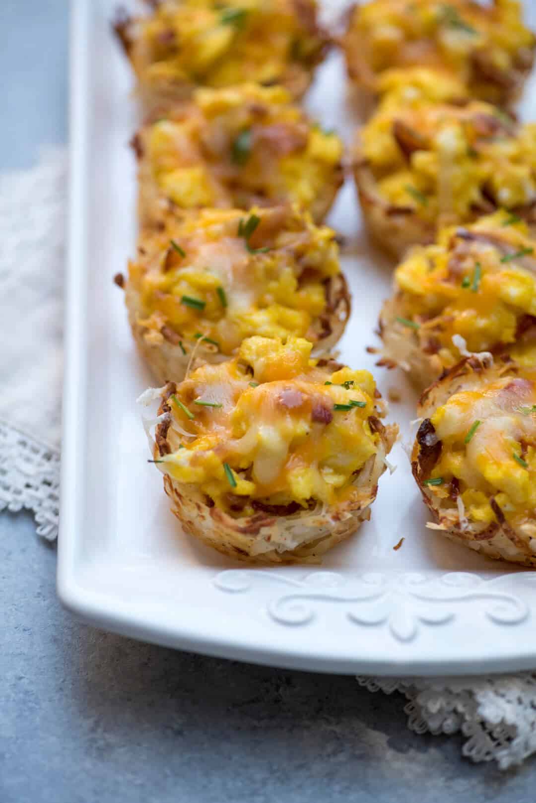 Muffin Tin Hash Brown and Scrambled Egg Cups lined up on a white serving tray.