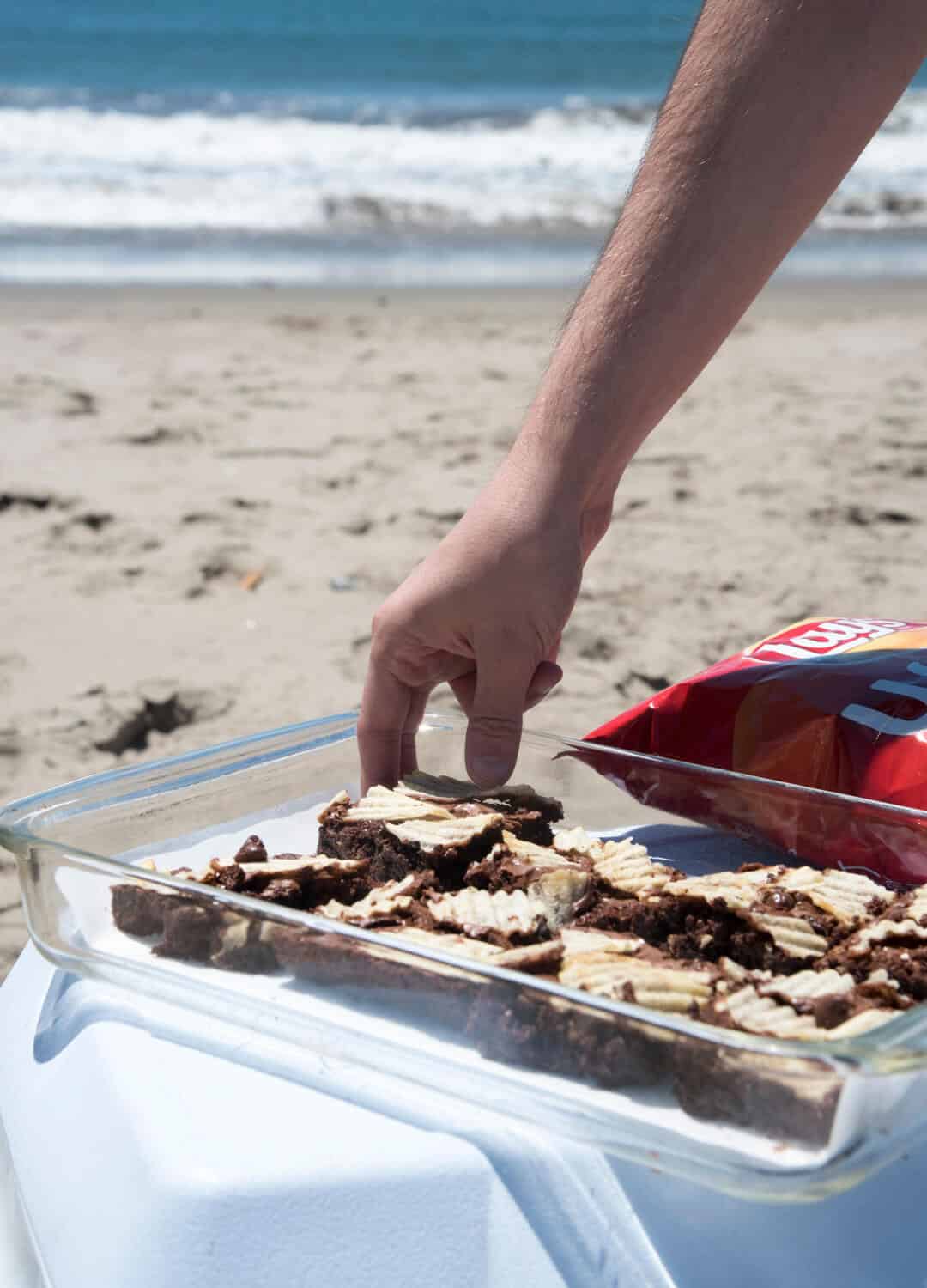 A hand reaches for a brownie in a baking dish.