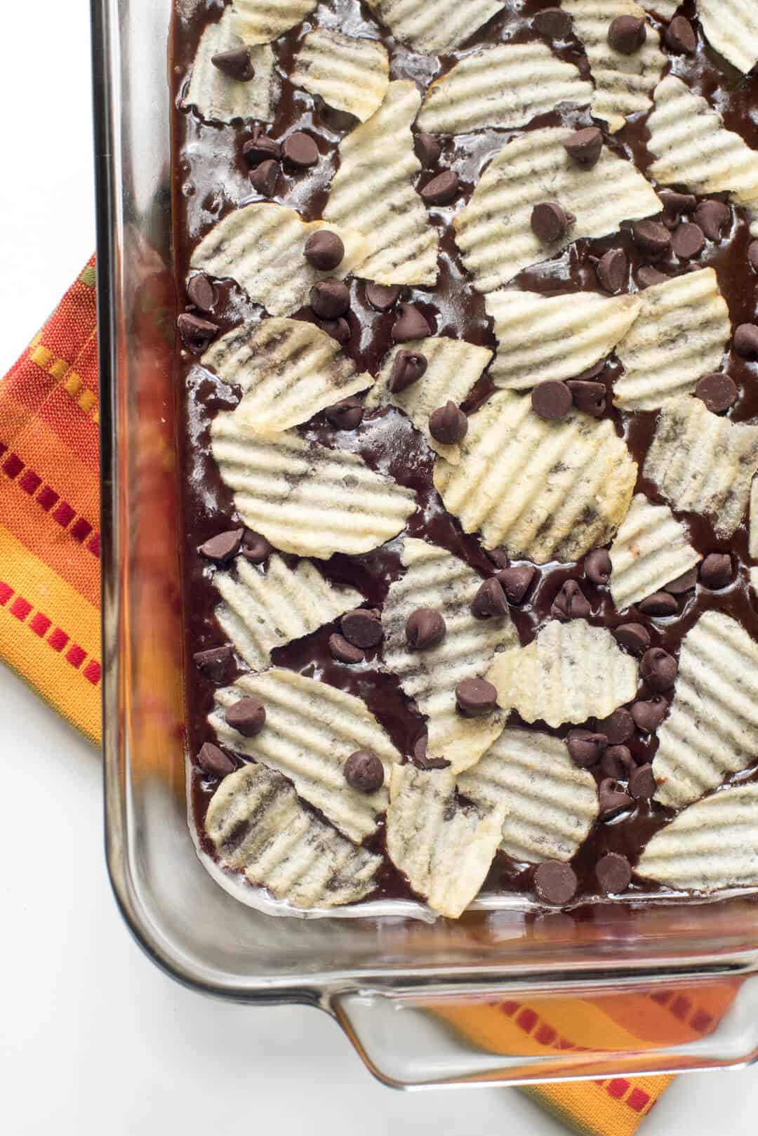 Brownie batter topped with potato chips and chocolate chips in a baking dish.