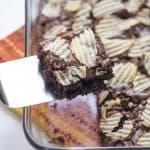 A spatula lifts a brownie topped with potato chips from a baking dish.