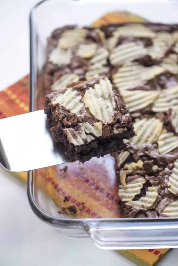 A spatula lifts a brownie topped with potato chips from a baking dish.