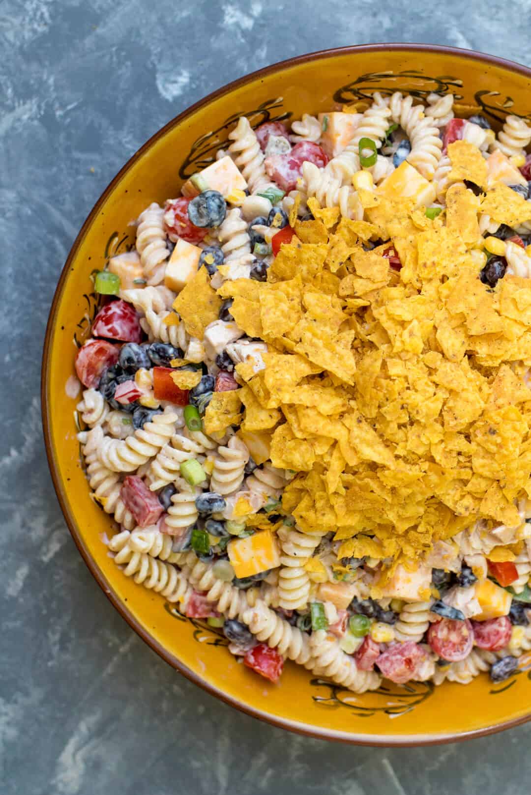 A close up over the top shot of the pasta salad topped with crushed Doritos in a large bowl.