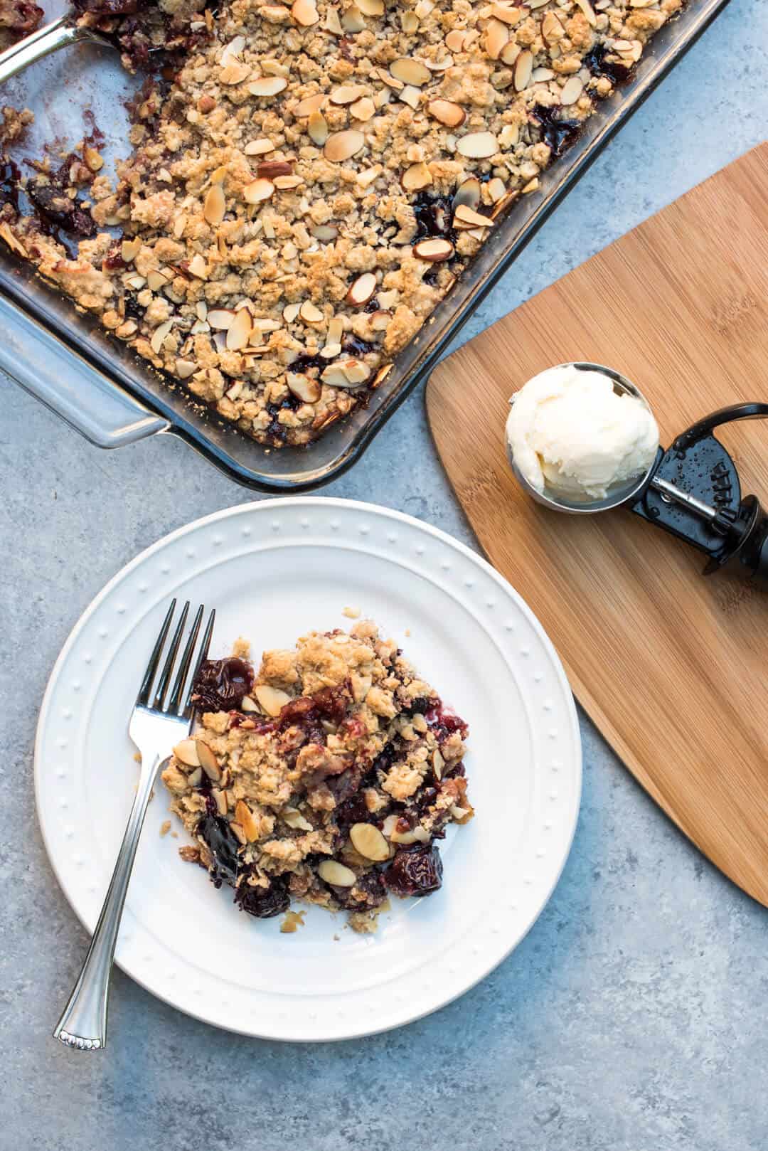 Cherry Crisp on a white plate with an ice cream scoop behind it.